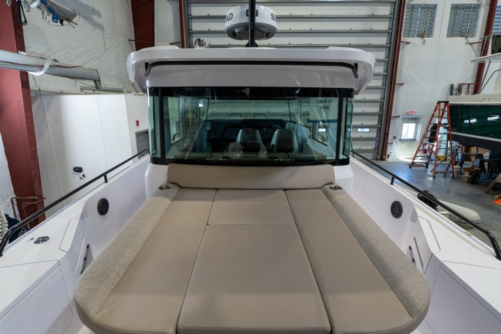 Front view of an Axopar 37’s aft cabin roof sunbed upholstered in Sandstone, filling the roof area with a wide lounging cushion and integrated cupholders while the boat sits indoors.