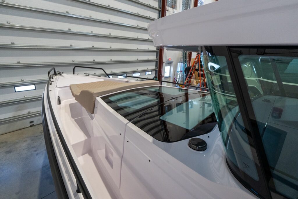Angled view along the side deck of an Axopar 37 inside a workshop, showing the tall cabin windows, the flush glass skylight panels on the cabin roof, and a small Sandstone cushion near the aft end.