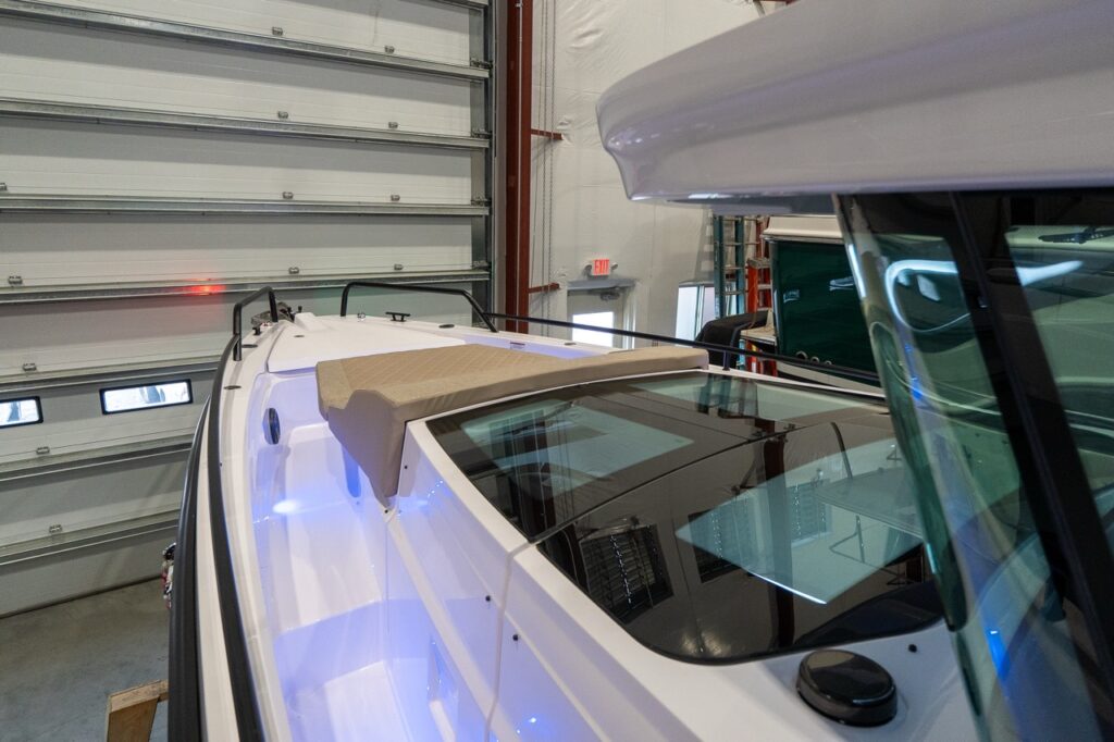 High, angled view along the starboard side deck of an Axopar 37 XC Cross Cabin, showing a Sandstone-colored foredeck sunpad positioned above the tinted glass roof panels of the forward cabin, with blue courtesy lighting along the side deck.
