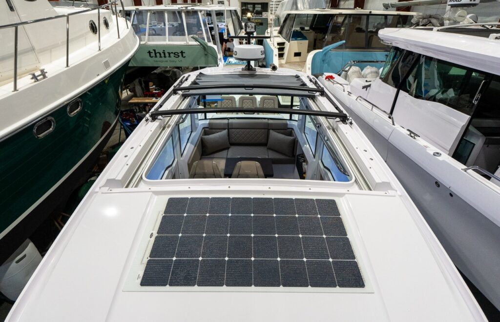 Top-down view of an Axopar 37 XC showing a large solar panel mounted on the roof and the open sun roof section over the cabin, revealing the aft lounge seating below inside a boat shed.