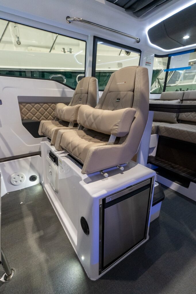 Axopar 37 XC Cross Cabin dual helm seats in Sandstone upholstery mounted above a stainless under-seat refrigerator in the pilothouse.