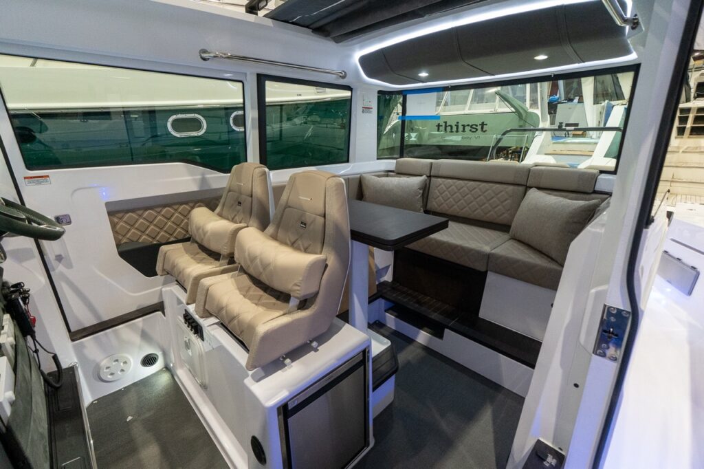 Axopar 37 XC Cross Cabin pilothouse interior with twin helm seats, dinette table, and aft lounge seating finished in Sandstone upholstery.
