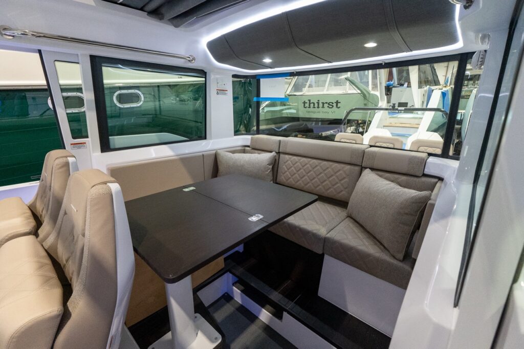 Axopar 37 XC Cross Cabin pilothouse dinette with a large dining table, wraparound lounge seating in Dust upholstery, and expansive side and aft windows.