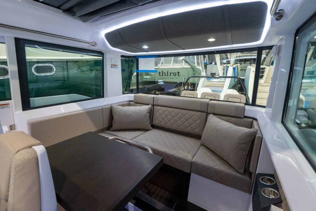 Axopar 37 XC Cross Cabin pilothouse dinette with wraparound seating, dining table, large windows, and Dust upholstery with quilted cushions and throw pillows.