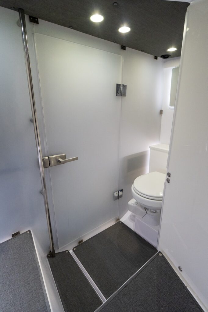 Axopar 37 XC Cross Cabin enclosed head compartment showing the privacy door, marine toilet, overhead recessed lighting, and non-slip flooring.