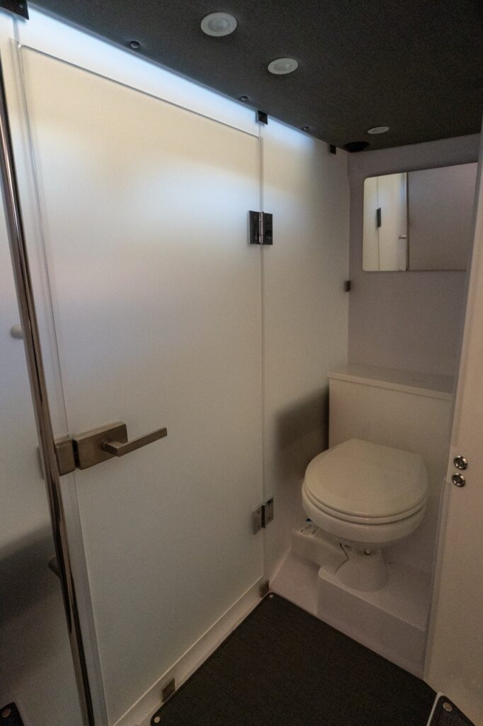 Axopar 37 XC enclosed head compartment showing the privacy door, marine toilet, mirror, and overhead lighting.