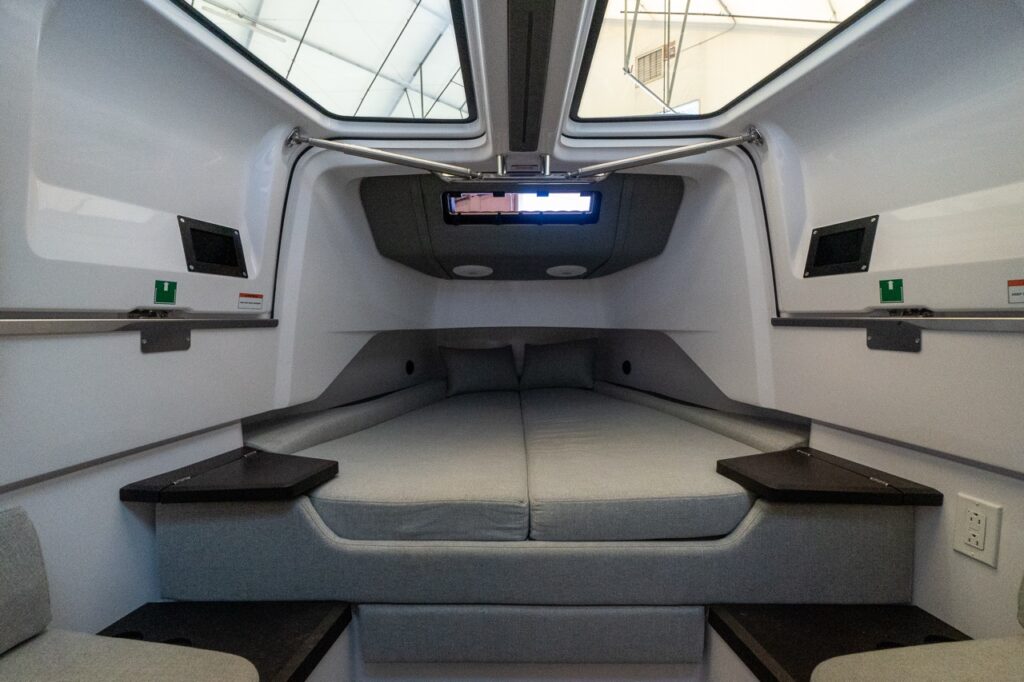 Axopar 37 XC forward cabin berths with the gullwing side doors open overhead, showing twin berth cushions, pillows, and built-in side shelves.