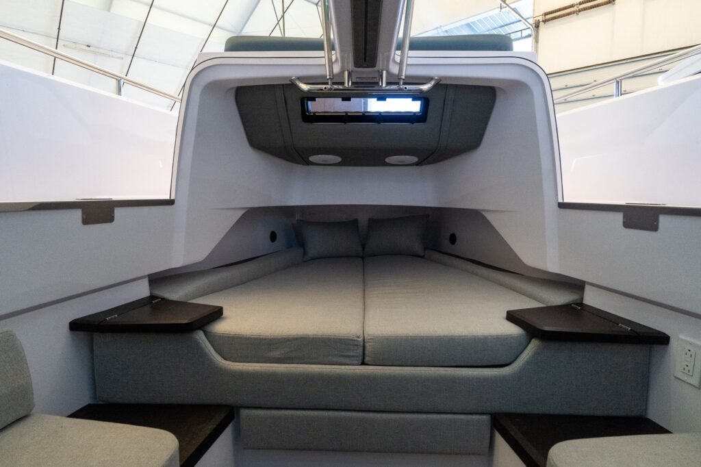 Forward cabin berths in an Axopar 37 XC Cross Cabin with twin cushions, pillows, side shelves, and the gullwing doors raised for light and ventilation.