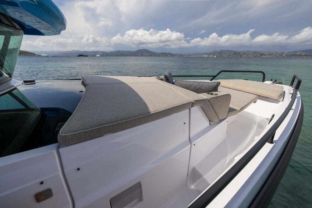 Foredeck sunpad and lounge cushions on an Axopar 37 XC beside calm water with mountains and clouds in the distance.