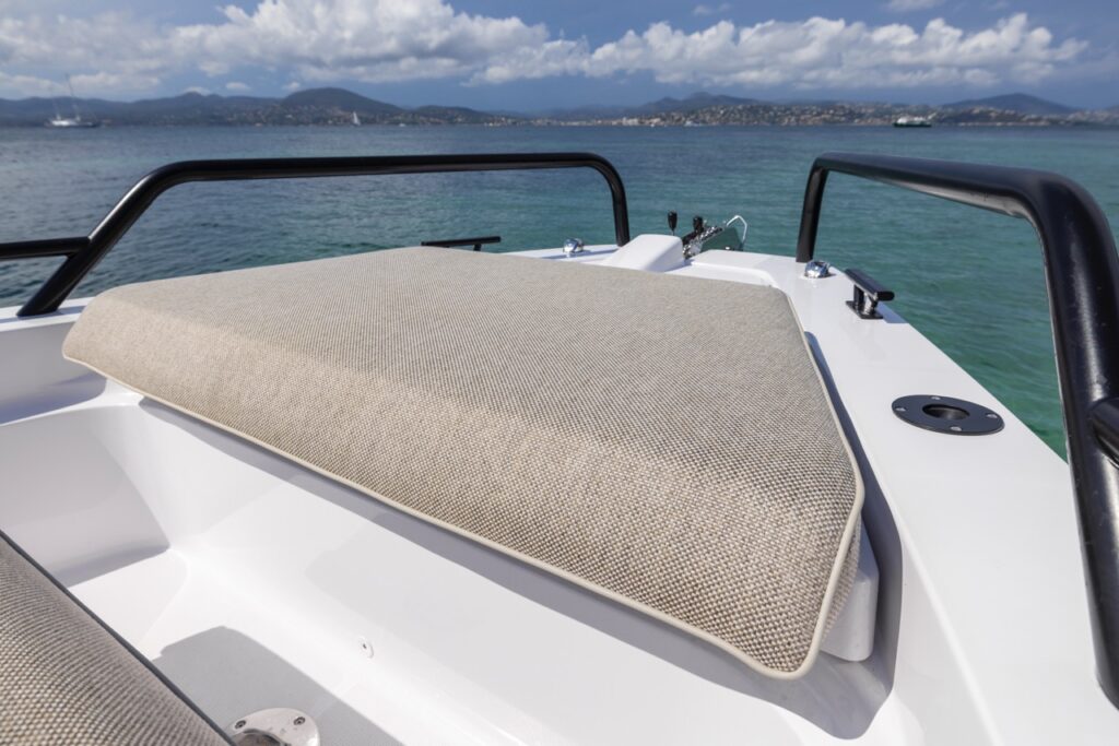 Axopar 37 XC foredeck sunpad cushion in Mediterrana upholstery on the bow, framed by railings with blue water and distant mountains in the background.