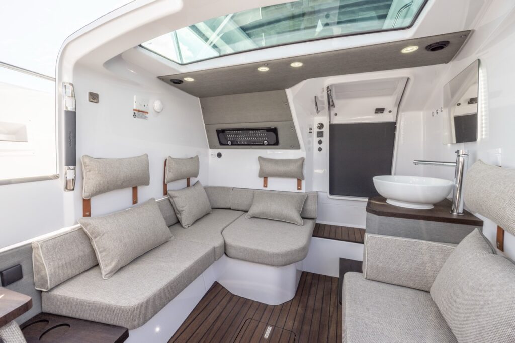 Axopar 37 XC Cross Cabin Mediterrana Edition forward cabin with wraparound lounge seating, pillows, skylight, and a compact vanity sink area to starboard.