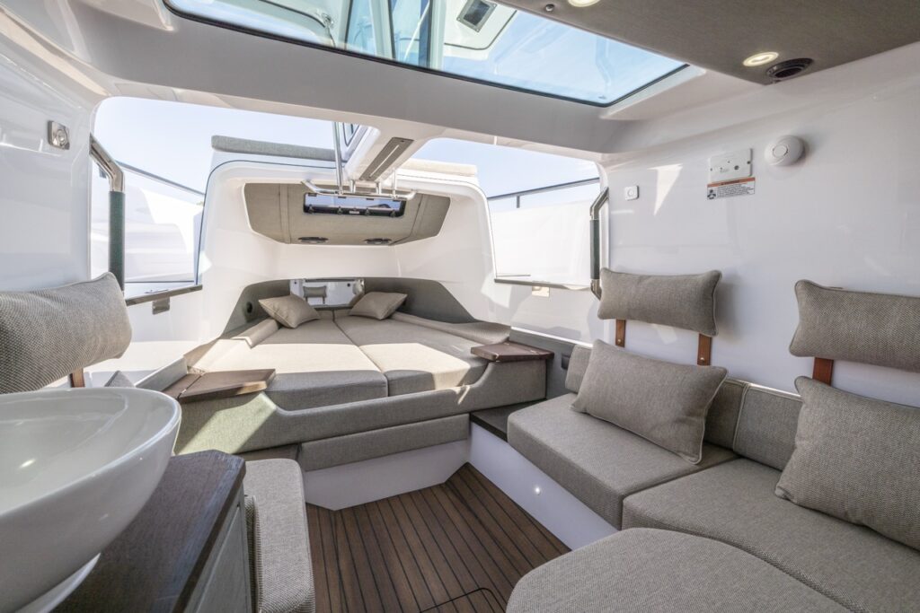 Axopar 37 XC Cross Cabin Mediterrana Edition forward cabin with gullwing doors open, skylight overhead, aft lounge seating, and forward berths with cushions and side shelves.