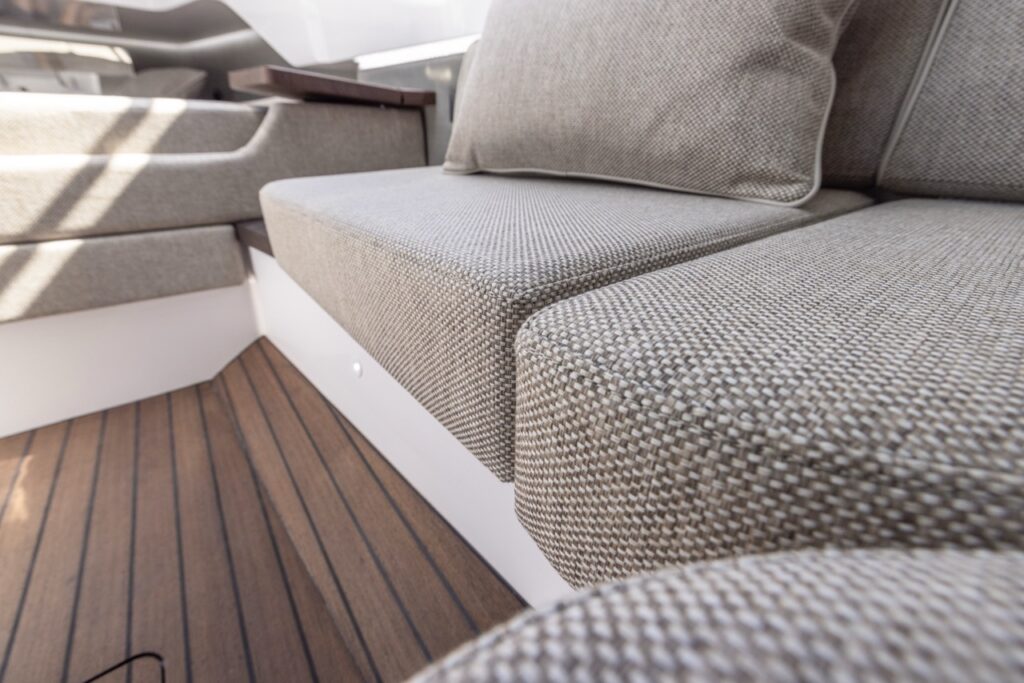 Close-up of Axopar 37 XC Mediterrana Edition cabin seating cushions with textured fabric upholstery, matching throw pillow, and teak-style cabin sole flooring.