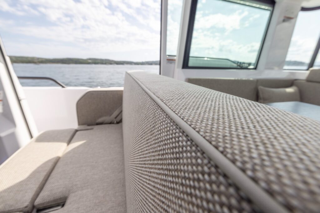 Close-up of Axopar 37 XC Mediterrana Edition pilothouse bench seat backrest showing textured Mediterrana upholstery and piping, with windows and water view in the background.