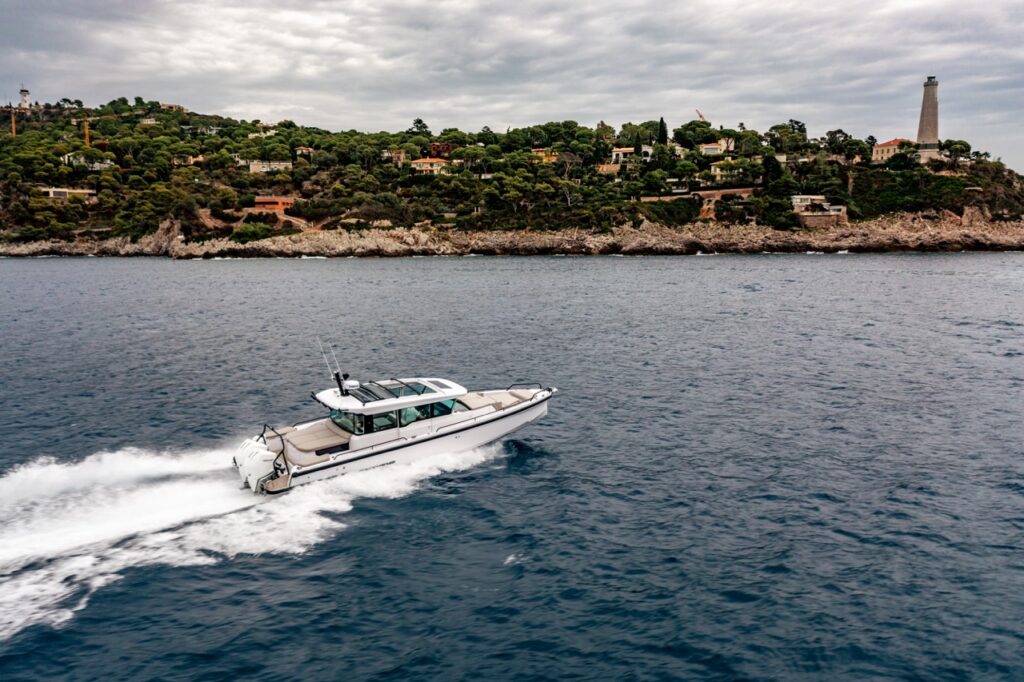 Axopar 37 XC Cross Cabin cruising at speed offshore with a wooded coastline and lighthouse in the background.