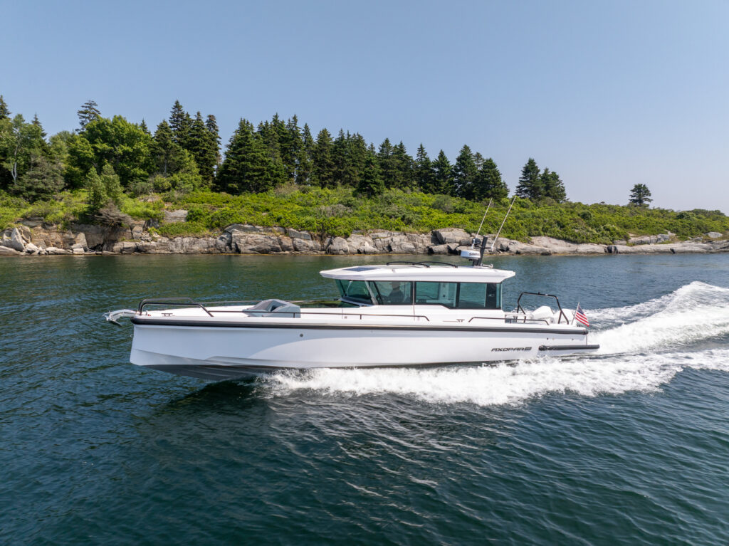 Axopar 37 cruising across the water in front of a rocky, green island on a clear day.
