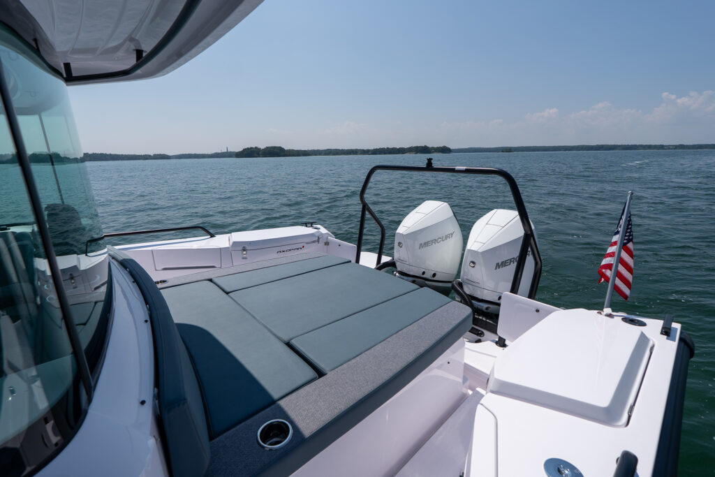 Aft sunbed and twin Mercury outboards on a 37 Axopar, floating on calm open water with an American flag at the stern.