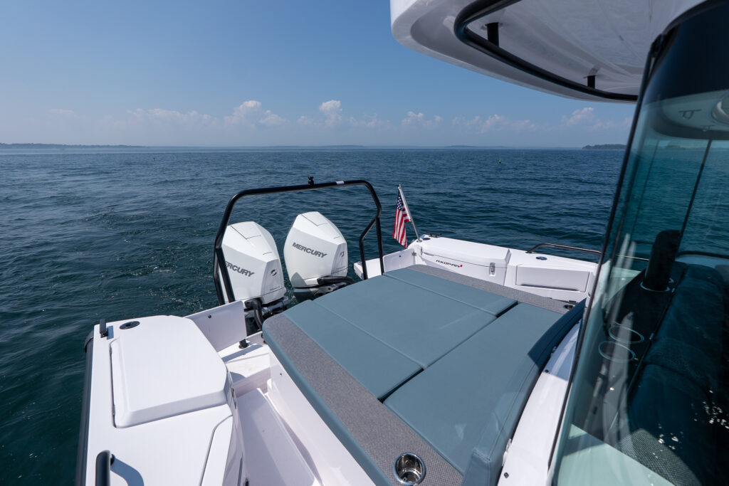Aft sunbed with petrol-colored upholstery on a 37 Axopar, positioned ahead of twin white Mercury outboards on open water.