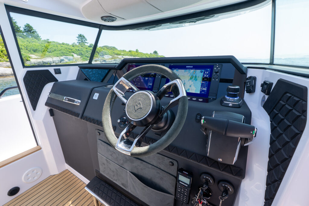 Helm of an Axopar 37 featuring a premium steering wheel, dual Simrad displays, Mercury throttle controls, joystick piloting, and black textured dash accents.