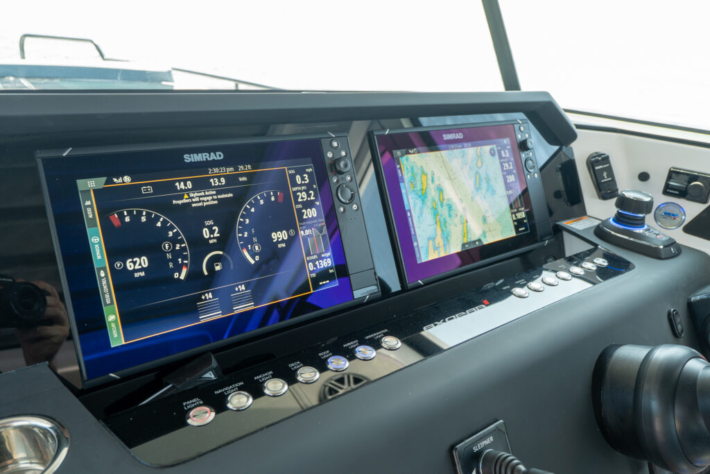 Dual Simrad multifunction displays on an Axopar 37 helm showing engine data, navigation charts, and system controls, alongside backlit switch panels and a Mercury joystick.