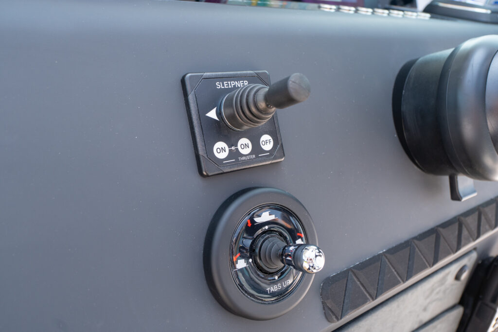 Close-up of the Axopar 37 helm showing a Sleipner thruster joystick and trim tab control knob mounted on a matte black dashboard.