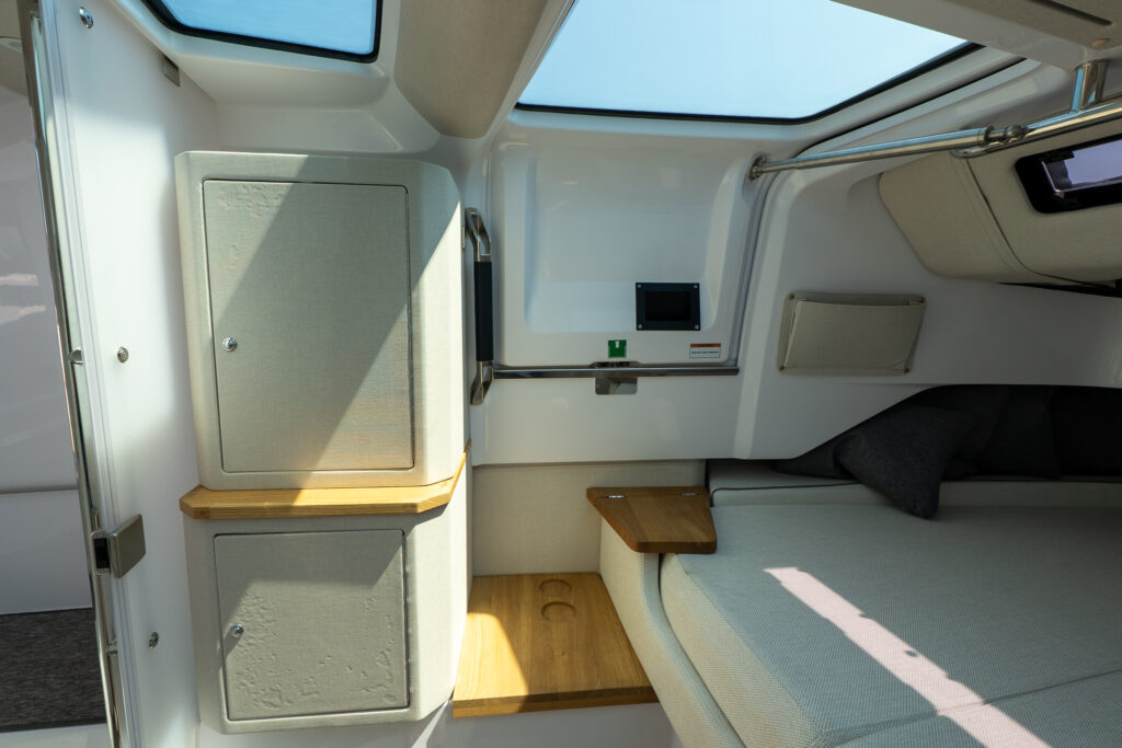 Forward cabin of an Axopar 37 showing storage cabinets, overhead skylights, cushioned berth, and built-in wooden shelving with cupholders.