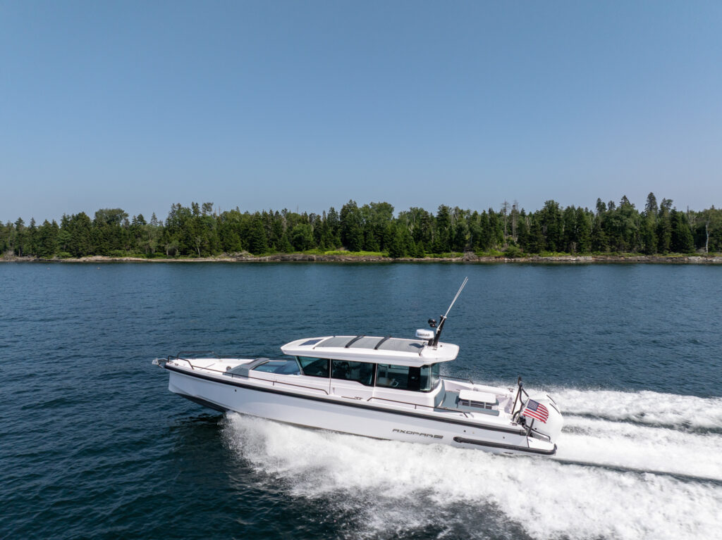 Axopar 37 cruising at speed along the coast of Casco Bay on a clear day. The overall scene conveys a sense of motion, clarity, and coastal adventure.