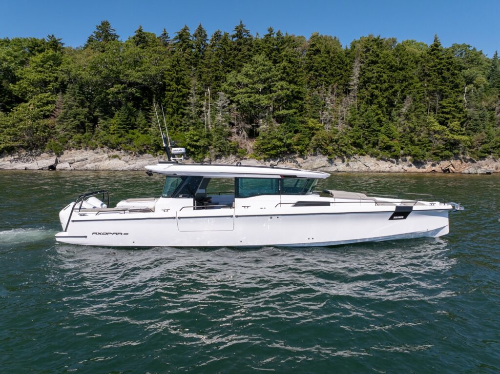 Axopar 45 BRABUS Performance Line cruising on Casco Bay, Maine with a forested rocky shoreline in the background.