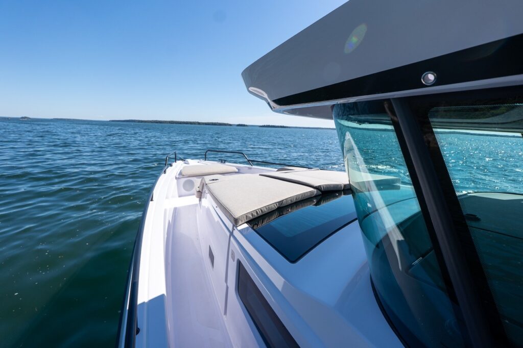 View forward along the starboard walkaround of an Axopar 45 BRABUS, showing the foredeck sunpad and windshield with open water ahead in Casco Bay, Maine.