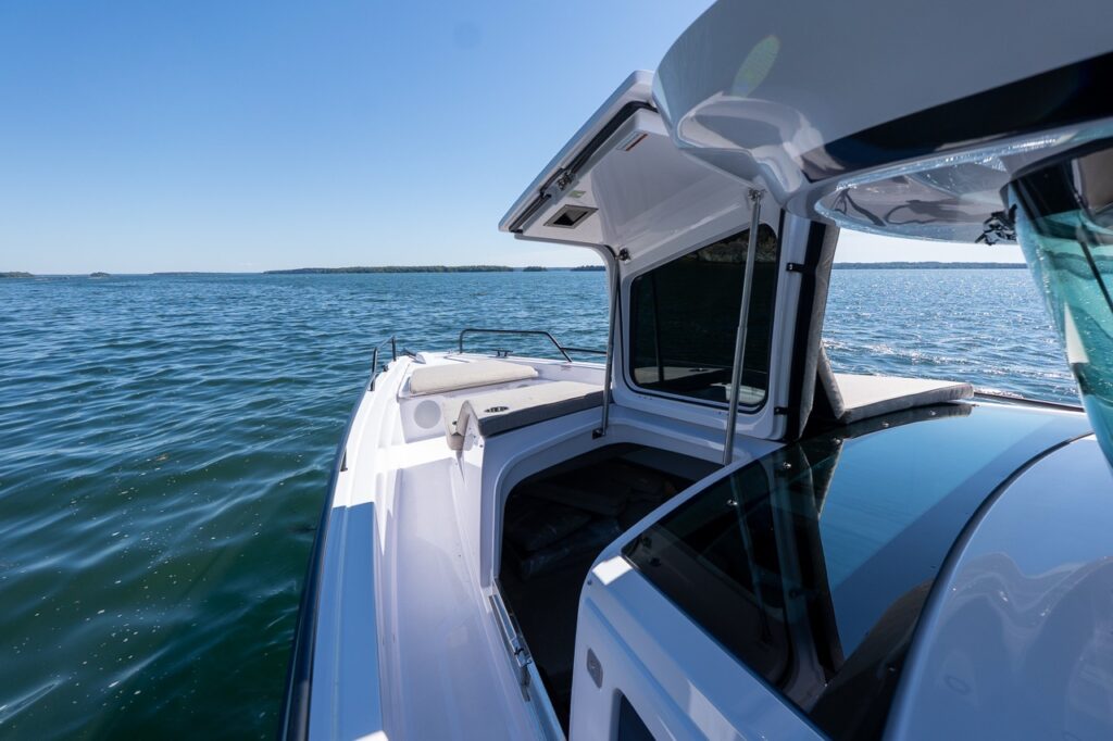 Starboard walkaround view on an Axopar 45 BRABUS with the foredeck storage hatch open beside the sunpad, cruising in Casco Bay, Maine.