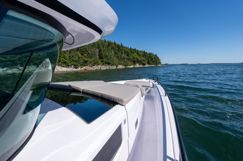 Port-side walkaround view on an Axopar 45 BRABUS Performance Line with the bow sunpad set up, cruising past rocky, tree-lined shoreline in Casco Bay, Maine.