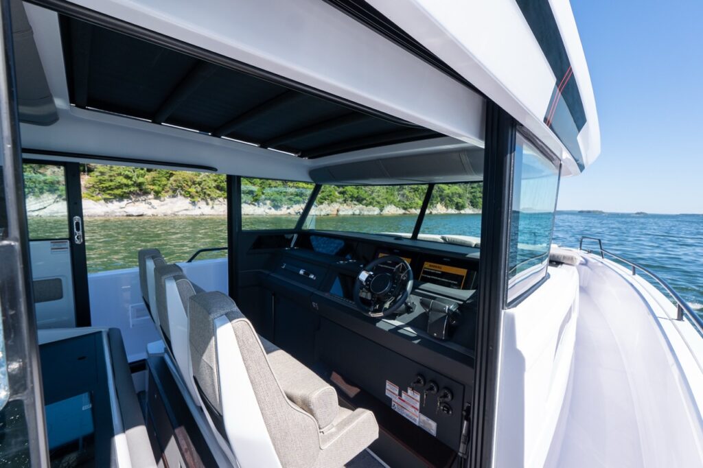 Open helm station on an Axopar 45 BRABUS Performance Line with twin seats, a Multi Function Display (MFD), and walkaround side deck beside the pilothouse in Casco Bay, Maine.