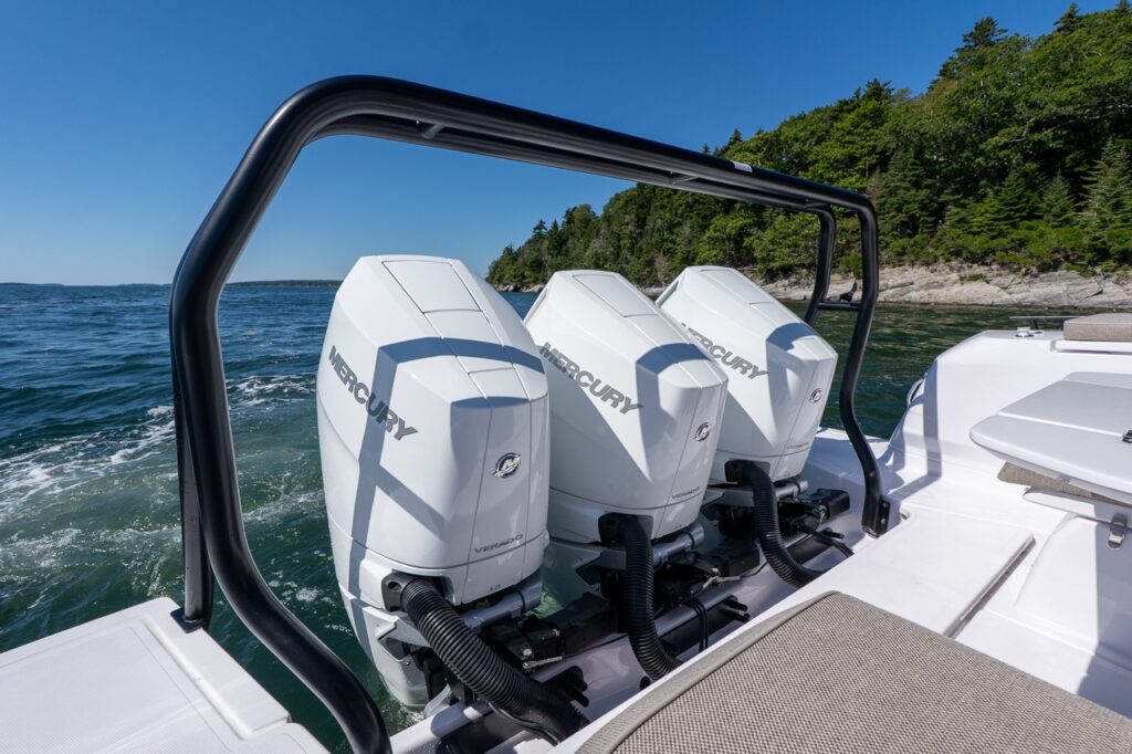Triple white Mercury Verado 350 outboards on the stern of an Axopar 45 cruising along a rocky Maine coastline.