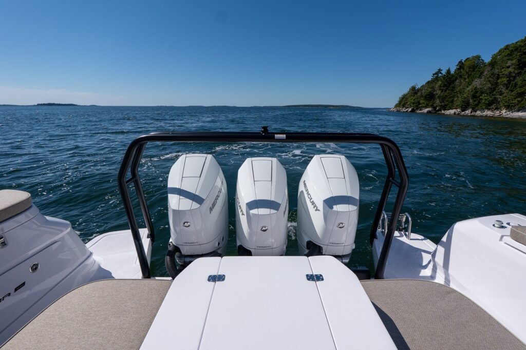 Rear-facing view of an Axopar 45 with triple Mercury Verado 350 outboards and a rocky Maine shoreline in the distance.