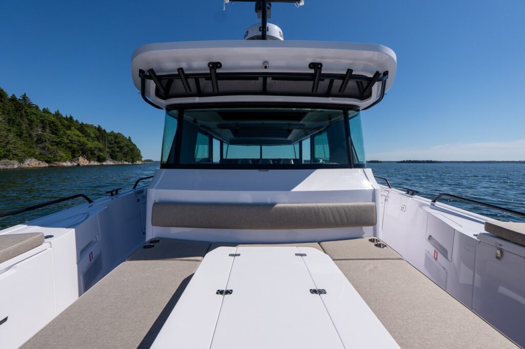 Looking forward from the stern on an Axopar 45 BRABUS Performance Line, showing the U-Sofa cockpit seating with table and the enclosed cabin windshield in Casco Bay, Maine.