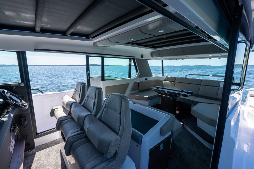 Interior view of the Axopar 45 BRABUS Performance Line showing aft salon lounge seating, helm chairs, and the Multi Function Display (MFD) with Casco Bay visible through the windows.