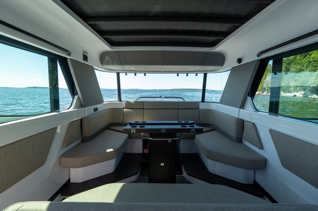 Aft cabin lounge seating area aboard an Axopar 45 BRABUS Performance Line with wraparound benches and a central table, looking out to Casco Bay, Maine.