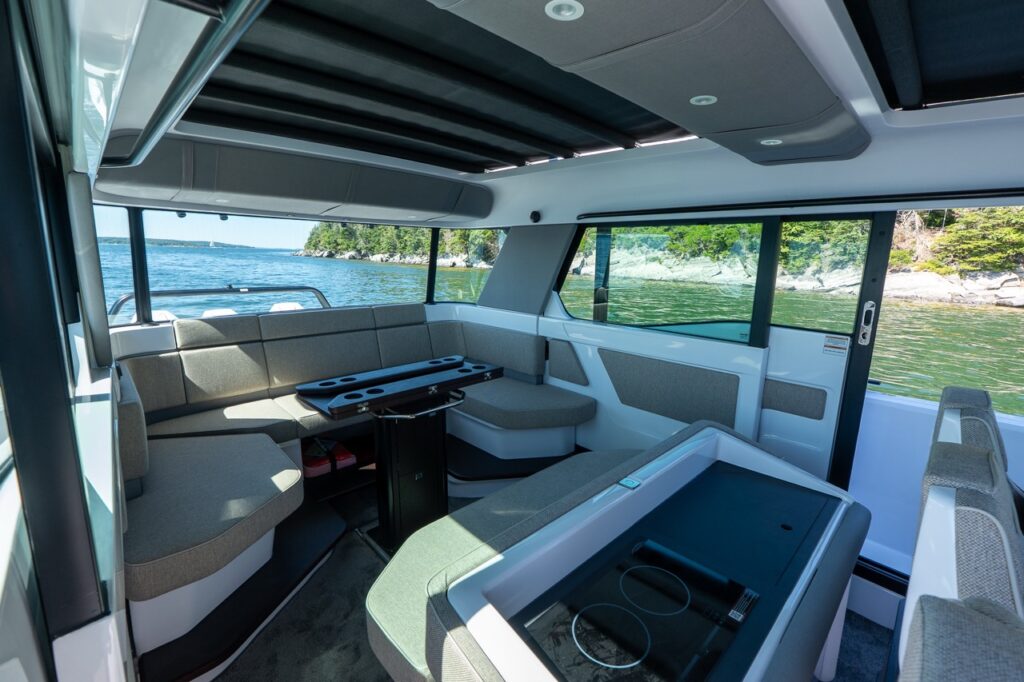 Interior cabin lounge on an Axopar 45 BRABUS Performance Line with wraparound seating, a central table, and panoramic windows overlooking Casco Bay, Maine.
