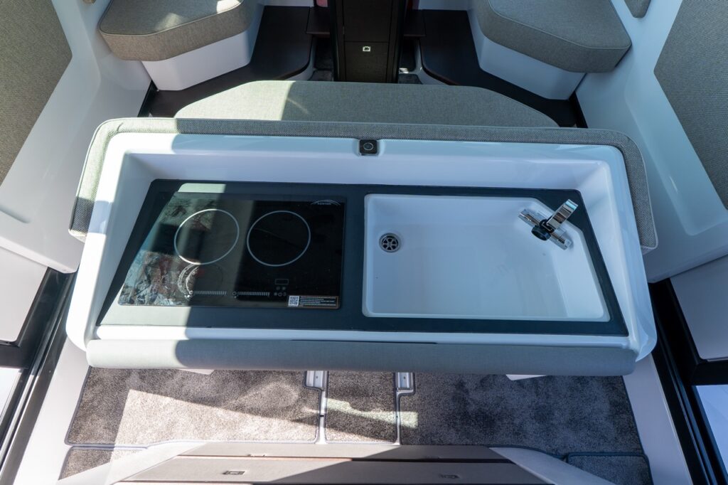 Top-down view of the Axopar 45 cabin galley with a two-burner cooktop beside a rectangular sink with a chrome faucet.