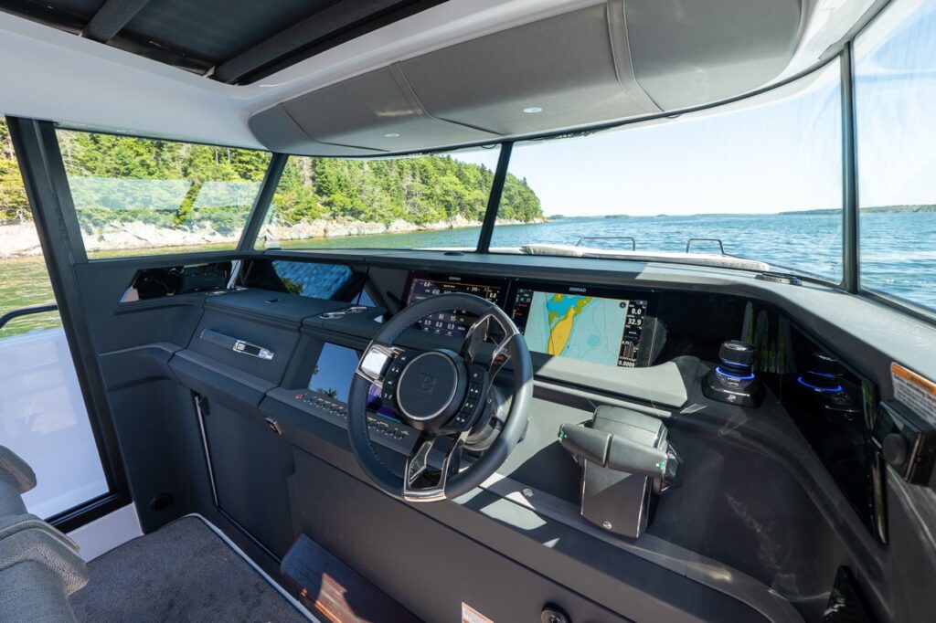 Helm area with a BRABUS steering wheel, twin Multi Function Display (MFD) screens showing charts and engine data, and throttle controls beneath a wide wraparound windshield.