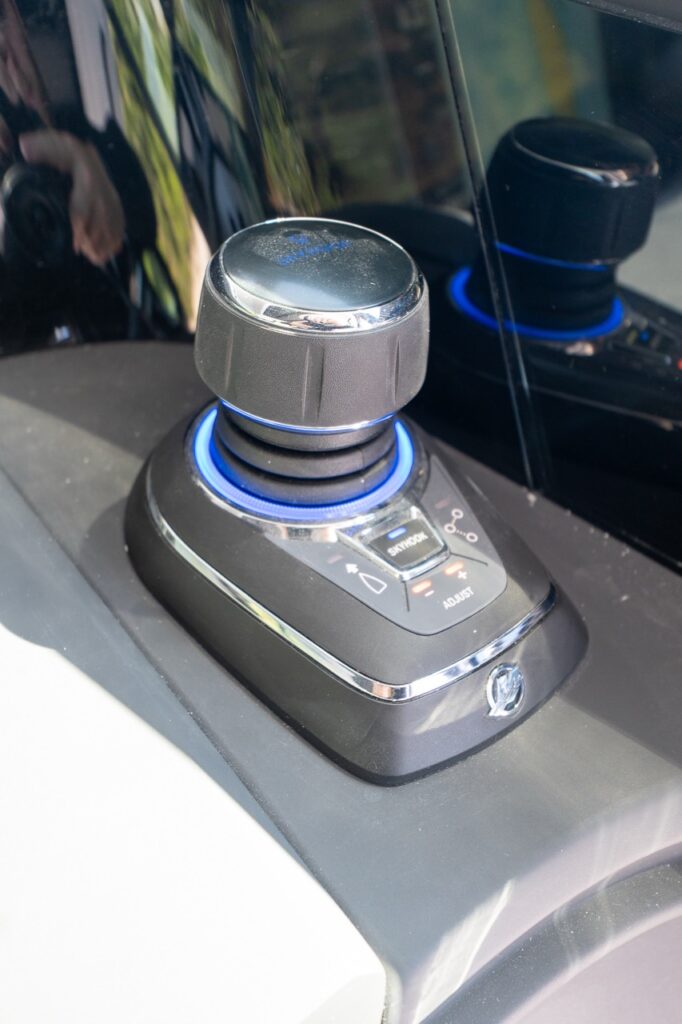 Close-up of the helm’s joystick docking and JPO control with an illuminated blue ring and integrated buttons on a glossy black console surface.