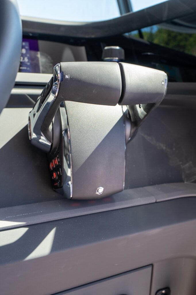 Close-up of a twin-lever throttle and shift control at the helm, with neutral “N” markings on each handle and a Multi Function Display (MFD) blurred in the background.