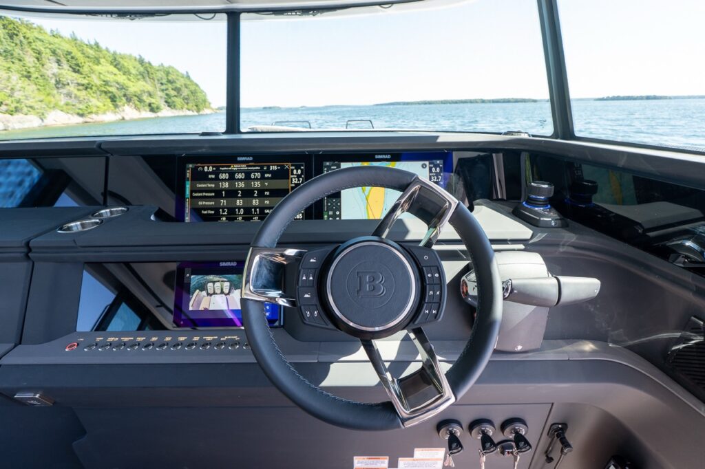 Helm station with a BRABUS-branded steering wheel, twin Multi Function Displays (MFDs) showing engine data and navigation, plus a joystick docking/JPO control and throttle levers, with open water visible through the windshield.