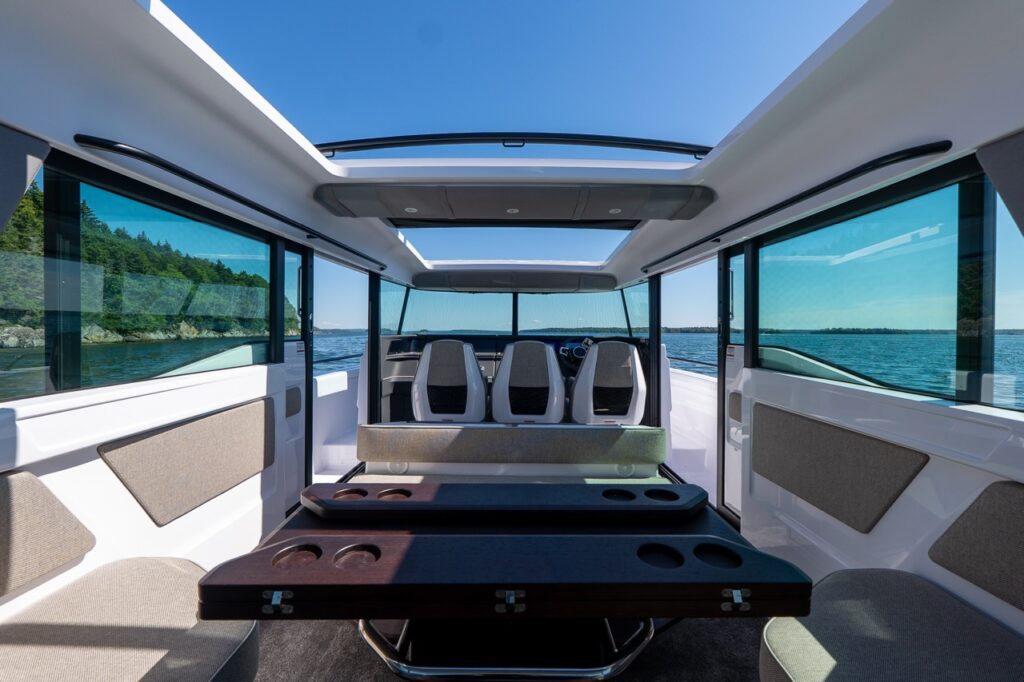 View forward through the Axopar 45 pilothouse with both sunroofs and the port and starboard side doors open, showing the dinette table, wide windows, and the helm seats ahead with open water beyond.