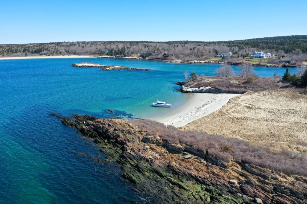Drone photo of an Axopar 37 XC Cross Cabin beached in a sheltered sandy cove with rocky shoreline and clear turquoise water, demonstrating safe beaching technique.