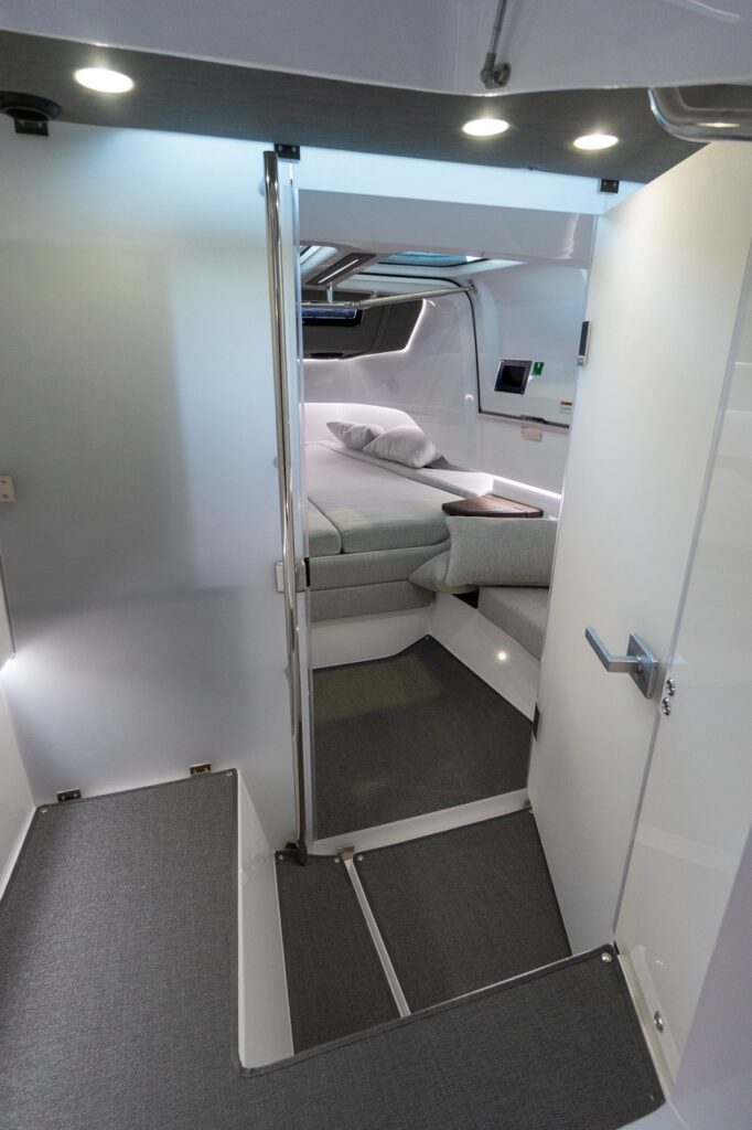 View through the Axopar 37 XC cabin doorway showing the entry steps and the forward cabin berth with integrated side seating and accent lighting.