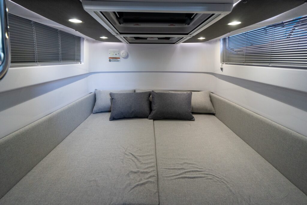 Axopar 37 XC aft cabin berth with large double sleeping surface, side cushions, reading lights, and window blinds.