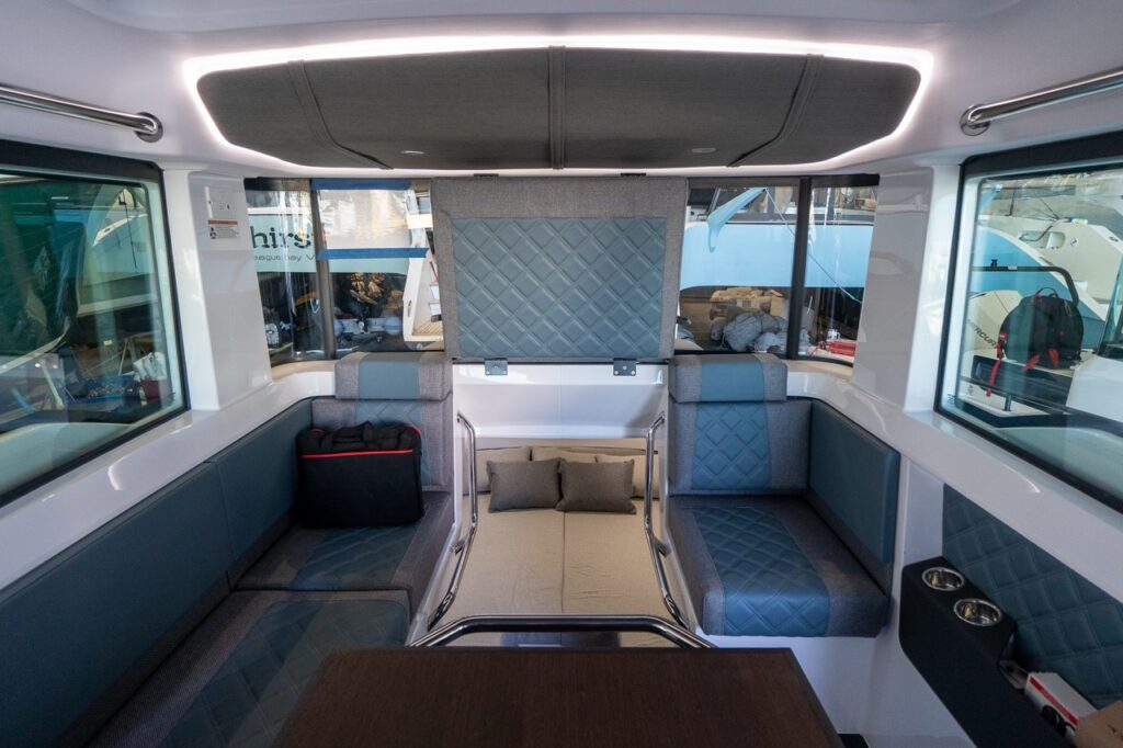 Interior cabin lounge of an Axopar 37 with U-shaped seating in blue quilted upholstery and a central berth area with cushions beneath a raised backrest.
