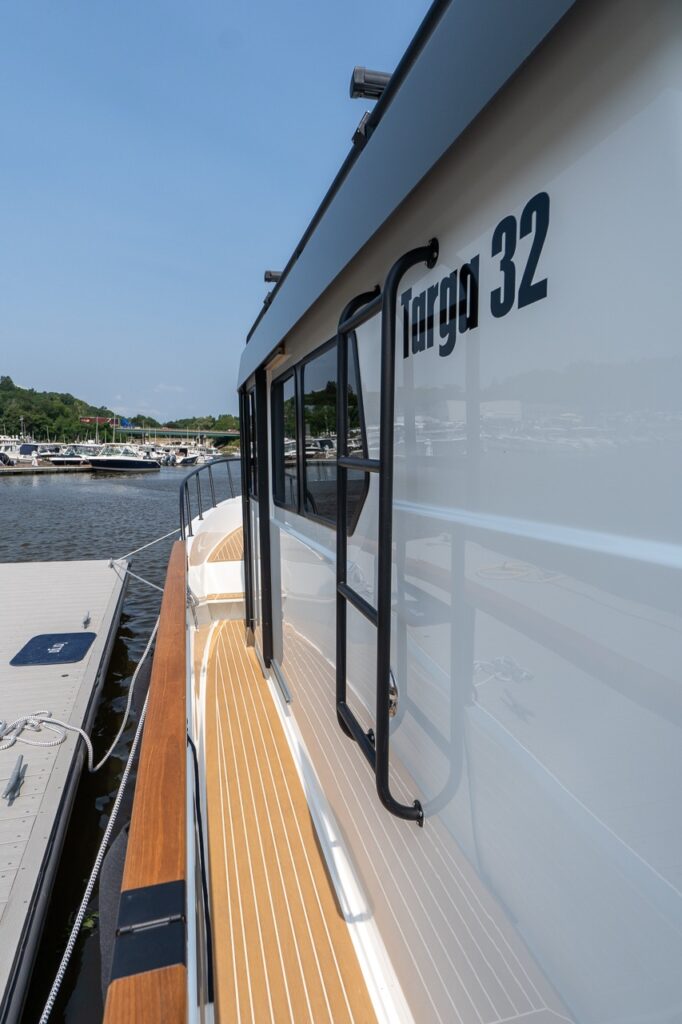 Port side deck of the Targa 32 showing the protected walkway with teak-style decking, side windows, and a fixed exterior grab ladder along the pilot house.