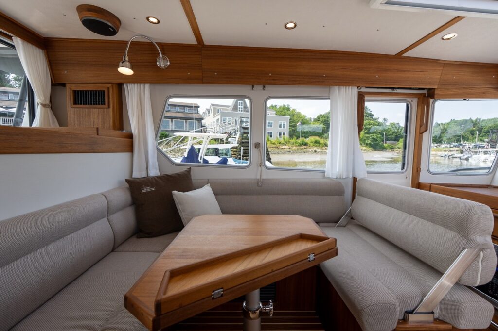 Portside dinette seating area in the Targa 32 pilot house with wraparound upholstered benches, a wood table, and large side windows.